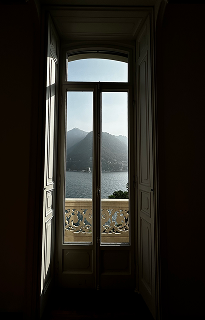 An open balcony door in the villa, framing Lake Como and the mountains beyond.