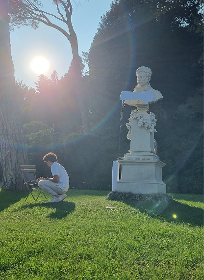 The final demo at golden hour: the laptop driving the piece on a folding chair, the bust lit from behind.
