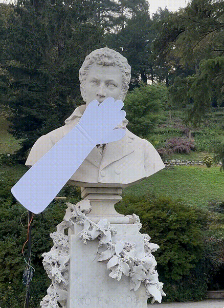 The marble bust of Ugo Foscolo in the garden, a pale cardboard arm raised across its face.